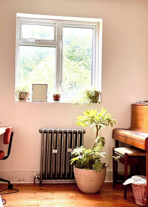 A room with a radiator, a piano, a window with plants, and a chair. - Room-cozy Guest Room in Vibrant Brighton (Brighton)