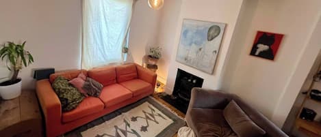 Een woonkamer met een bank, een vloerkleed, een kamerplant en een schilderij aan de muur.