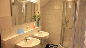 Ein Badezimmer mit zwei Waschbecken, einer Dusche, einem Spiegel und einer Vase mit Blumen.