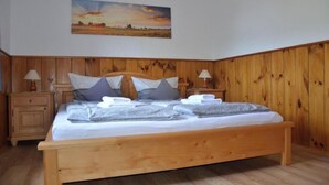 Ein hölzernes Bett mit Kissen und Decke, ein Nachttisch mit Lampe sowie ein Bild an der Wand.