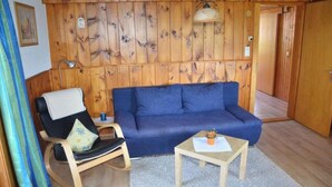Ein Zimmer mit Holzwänden, einem blauen Sofa, einem Schaukelstuhl und einem kleinen Holztisch.