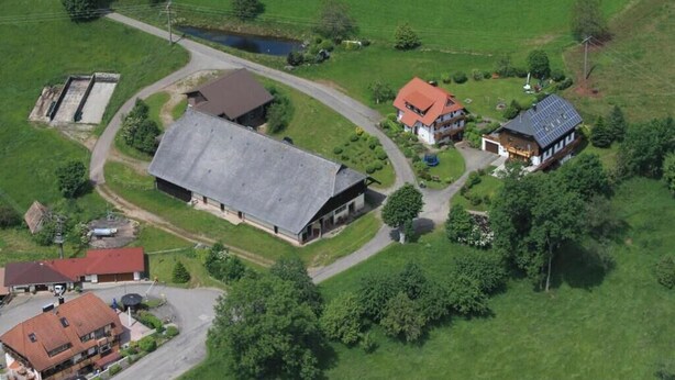 Ein Luftbild eines ländlichen Anwesens mit einer großen Scheune, einem Haus mit rotem Dach und umliegenden grünen Feldern.