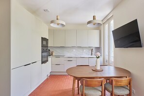 A modern kitchen with white cabinets, a dining table with chairs, a TV mounted on the wall, and pendant lights. - Apartment located in the heart of Aix-en-Provence (Saint-Antonin-sur-Bayon)