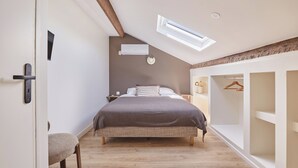 Une chambre avec un plafond en pente, un lit, une table de chevet, une lampe suspendue et une armoire.
