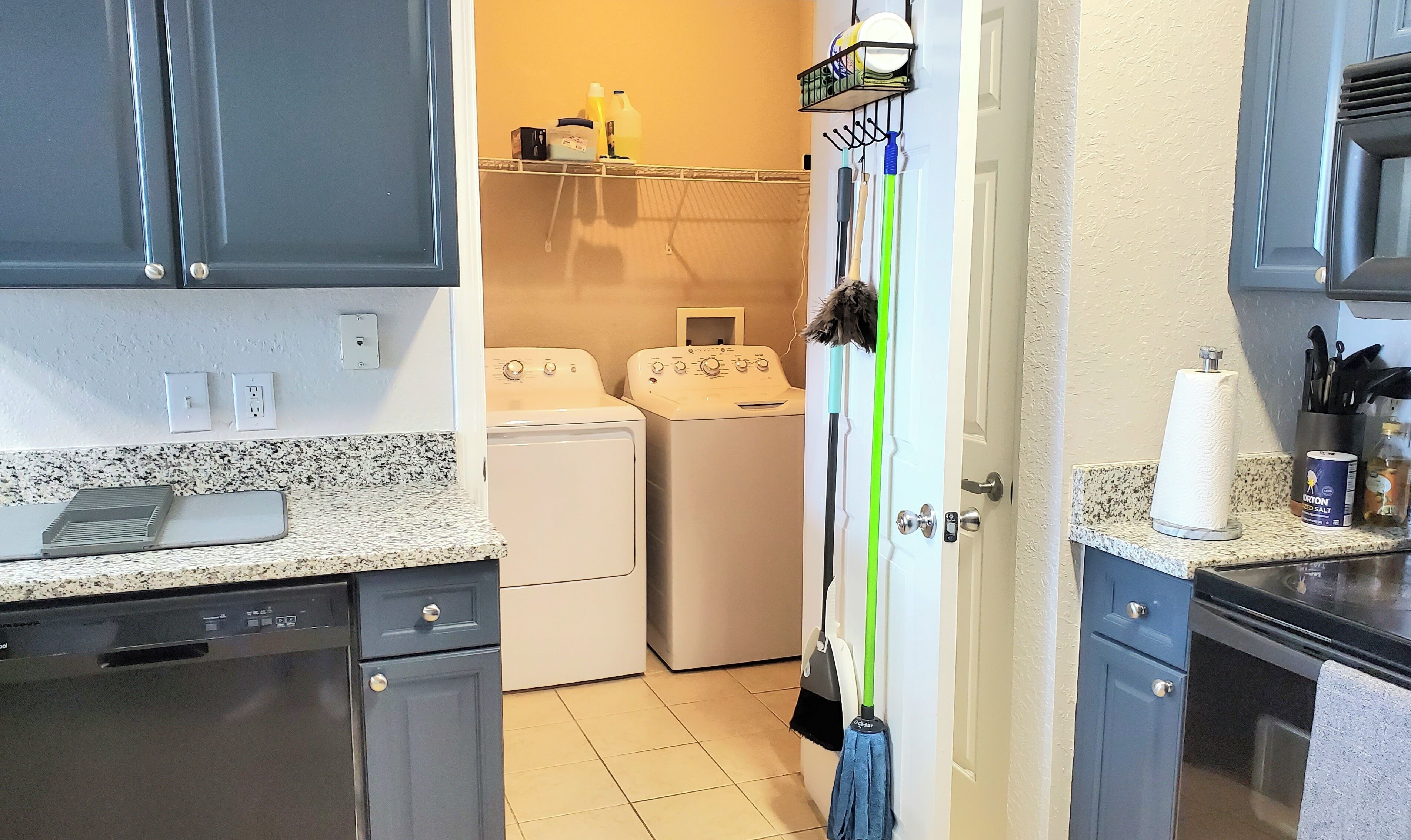 A kitchen with a dishwasher, a washing machine, and a mop leaning against the wall.