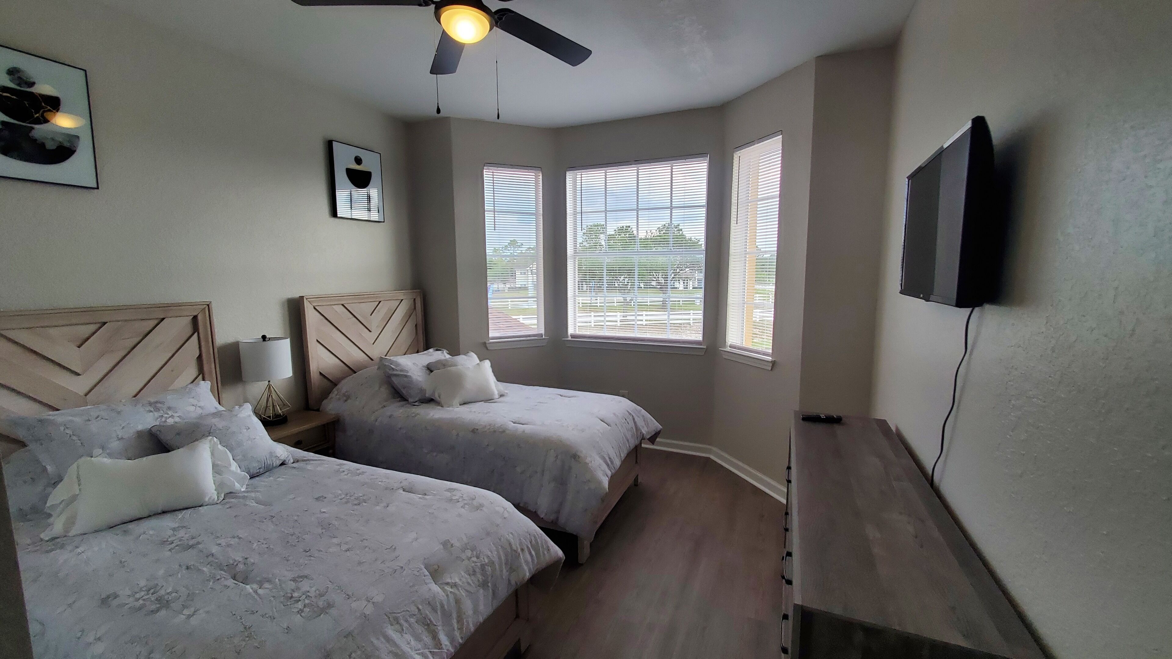 Un dormitorio con dos camas, ventilador de techo, televisor y ventanas con persianas.