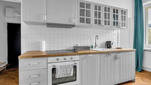 Una cucina con mobili bianchi, un piano di lavoro in legno, un fornello e una finestra con tende.