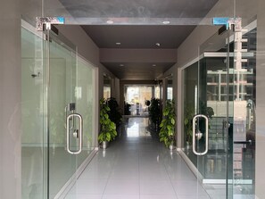 Um corredor moderno com portas de vidro, plantas em vasos e uma vista desobstruída para o interior do edifício.