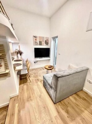 Un salon moderne avec un canapé gris, un plancher en bois, un téléviseur à écran plat et un coin repas comprenant une table et des chaises.