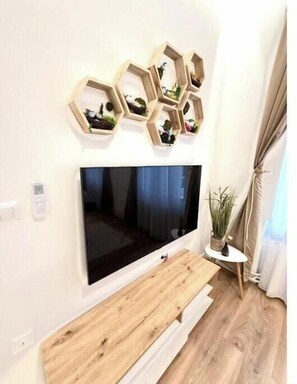 Ein modernes Wohnzimmer mit einem großen Flachbildfernseher an der Wand, einer hölzernen Sitzbank darunter und einem kleinen Beistelltisch mit einer Pflanze.