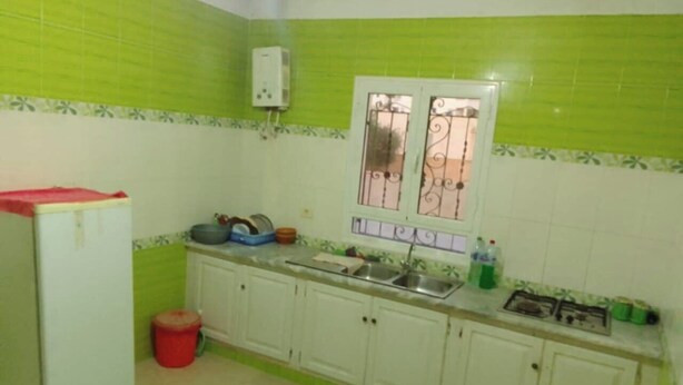 Cuina amb armaris blancs, una finestra amb baranes decoratives, un rentaplat i un frigorífic.