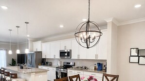 Una cocina moderna con armarios blancos, electrodomésticos de acero inoxidable y un comedor con mesa y sillas de madera.
