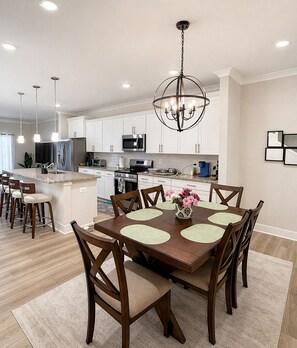 A modern kitchen with white cabinets, stainless steel appliances, and a dining area with a wooden table and chairs. - 3 En-Suite Beach House - 5 minutes Walk to Beach - Entire townhome - Sleeps 10 (Ocean City)