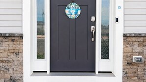 Una puerta principal oscura de color gris con un cartel de bienvenida, un buzón y un felpudo.