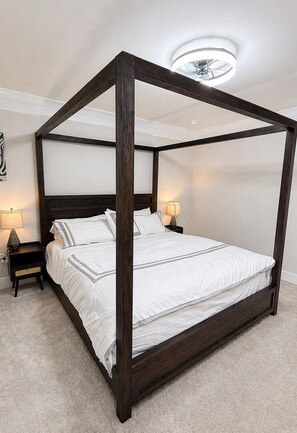 A four-poster bed with white bedding, two bedside tables with lamps, and a ceiling light fixture.