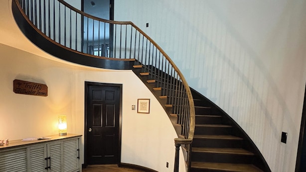 Un magnifique escalier avec des finitions en bois, une rampe noire et un mur blanc surmonté d’une porte.