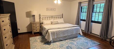 A bedroom with a bed, dresser, nightstand, lamp, ceiling fan, and windows with curtains.