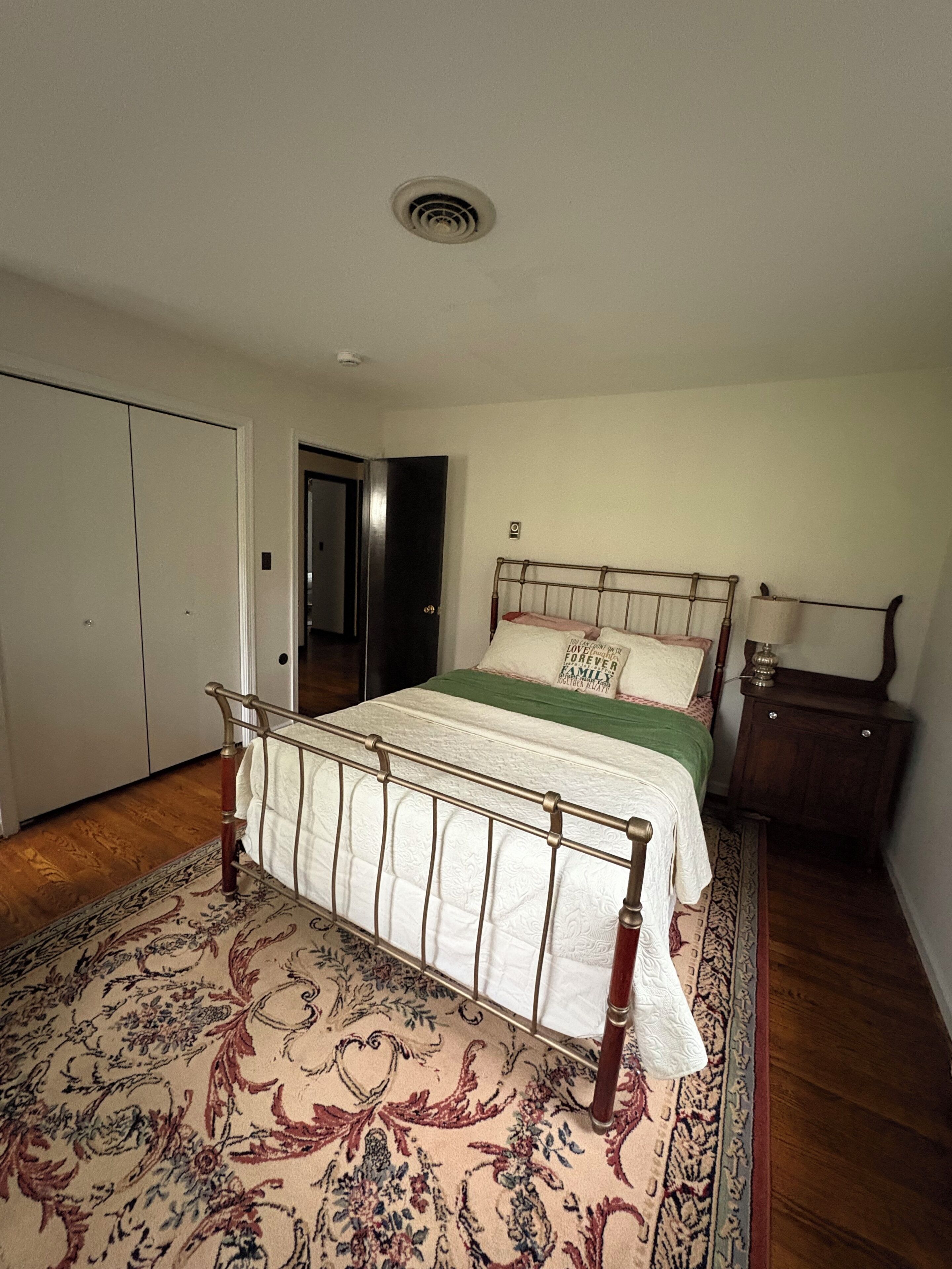 A bedroom with a bed, a nightstand, a lamp, a door, and a patterned rug.