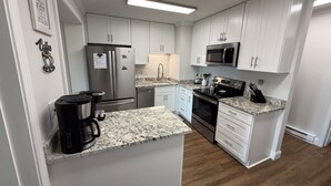 Eine moderne Küche mit weißen Schränken, einem Edelstahlkühlschrank, einer Mikrowelle und einer Kaffeemaschine.