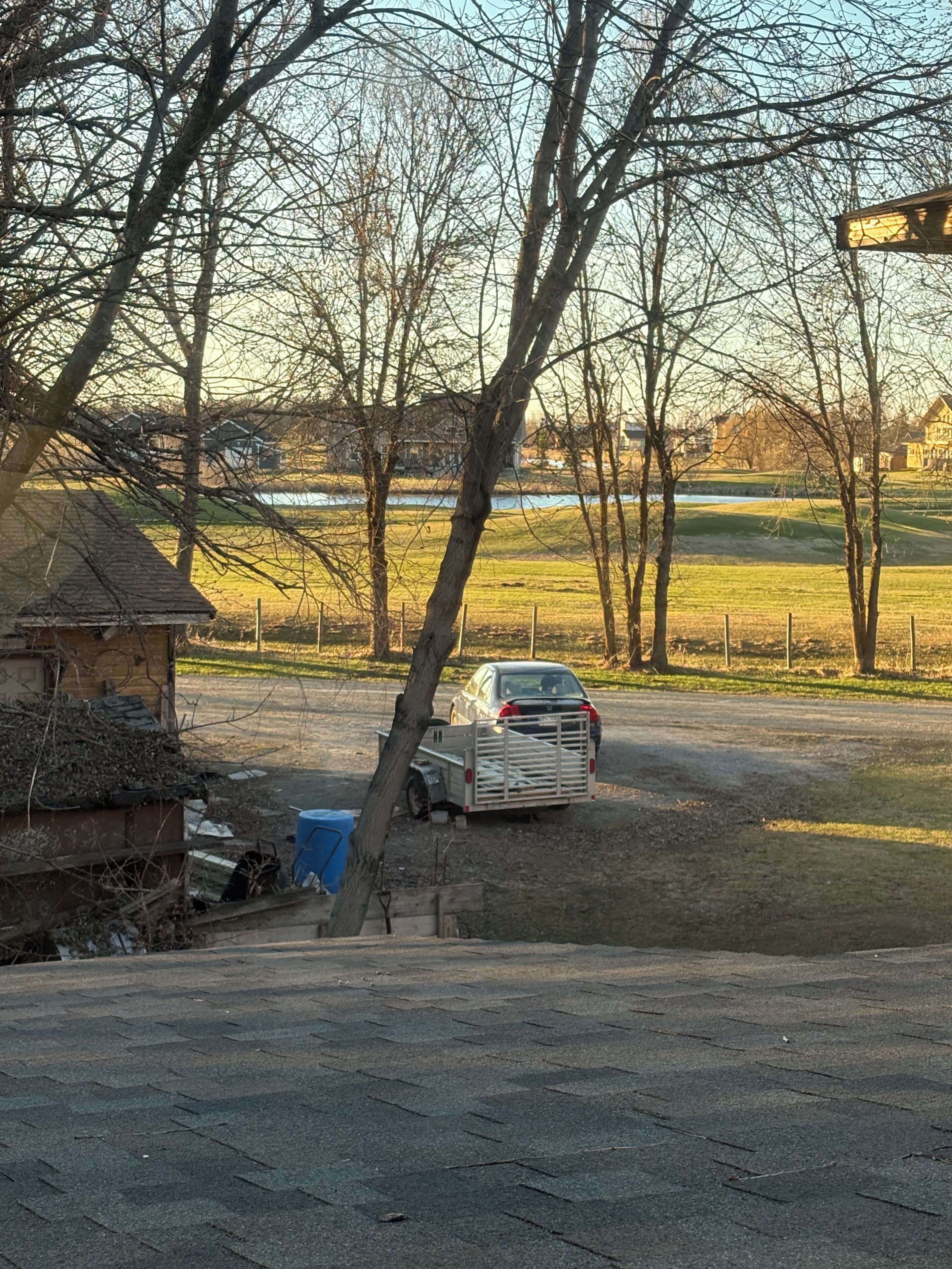 A parking area with a vehicle, trees, and a building in the background.