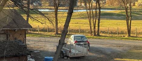 A parking area with a vehicle, trees, and a building in the background.