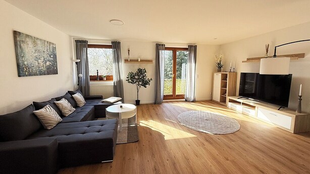 En moderne stue med en hjørnesofa, et fladskærms-tv, et sofabord og en potteplante.
