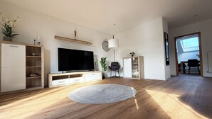 En moderne stue med et fladskærms-tv, trægulv, en rund måtte og en loftlampe.