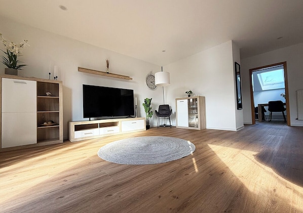 Una sala de estar moderna con un televisor de pantalla plana, suelo de madera, un tapete redondo e iluminación en el techo.