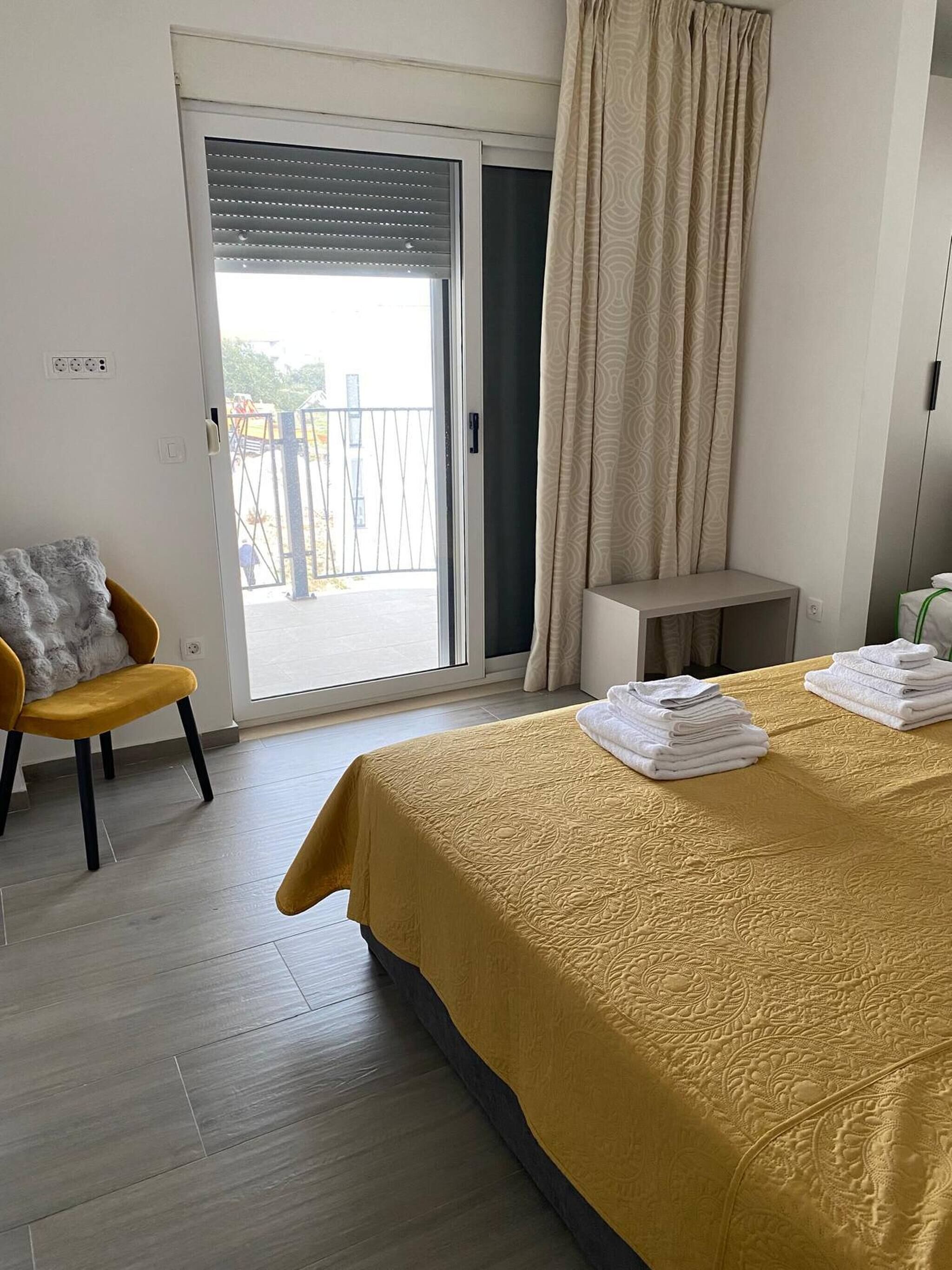 Habitació d'hotel amb un llit, una cadira, una taula petita i una vista per una porta corredissa.