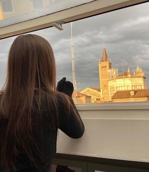 A person looking out of a window at a building with a prominent tower. - Bright apartment in the center of Parma- House Cavour 24 (Parma)