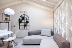 Ein modernes Wohnzimmer mit einem Ecksofa, einem Esstisch mit Stühlen, einer hängenden Leuchte und einem Wandregal für Pflanzen.