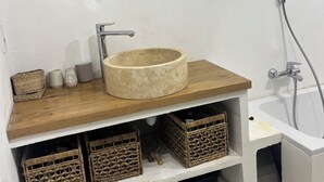 Un bagno con uno specchio rotondo, un mobile bagno in legno, una vasca da bagno e cesti in vimini.