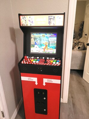 Ein rotes Spielautomaten-Gehäuse mit einem Bildschirm, der ein Kampfspiel zeigt, inklusive zwei Spieleroptionen und einem Münzeinslot.