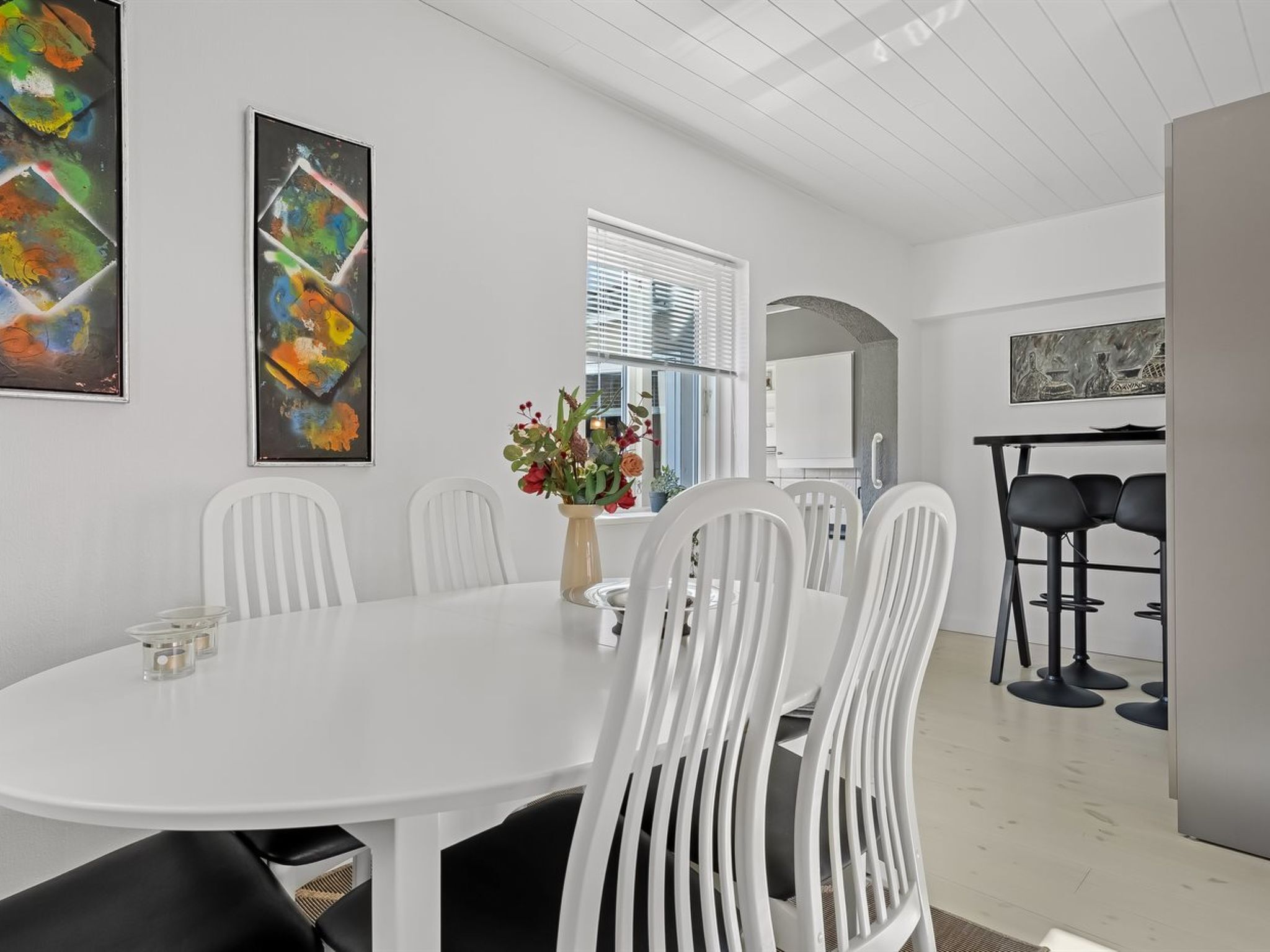 A modern dining area with a white table and chairs, a vase with flowers, and abstract art on the walls.