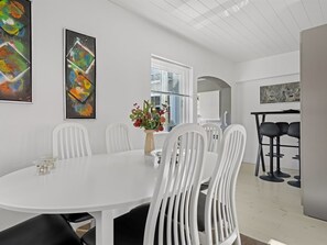 Et moderne spiseområde med et hvidt bord og stole, en vase med blomster og abstrakt kunst på væggene.