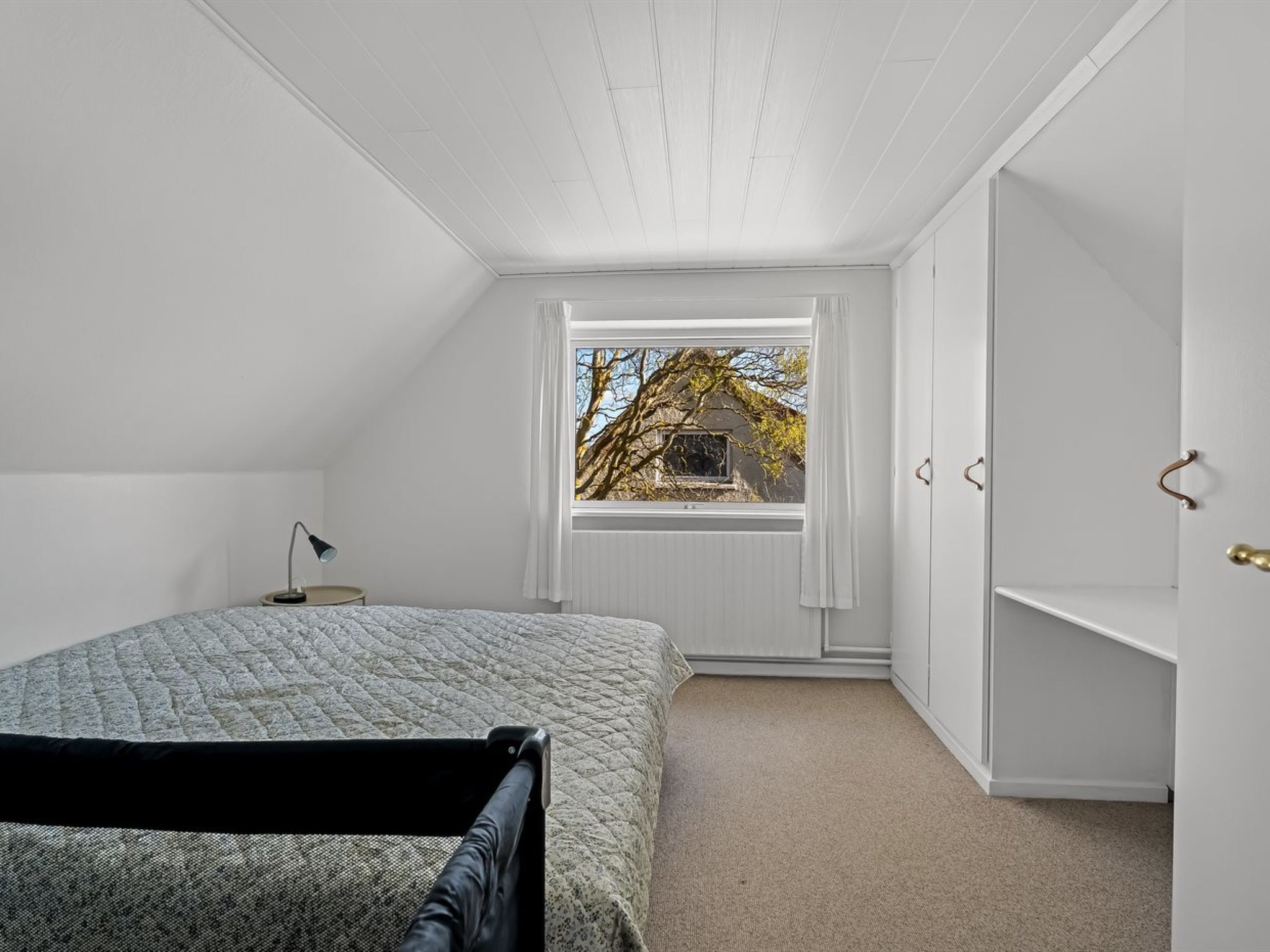 A bedroom with a bed, a desk, and a wardrobe.