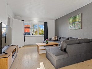 En moderne stue med en grå sofa, et træbord og et fjernsyn på et træstel.