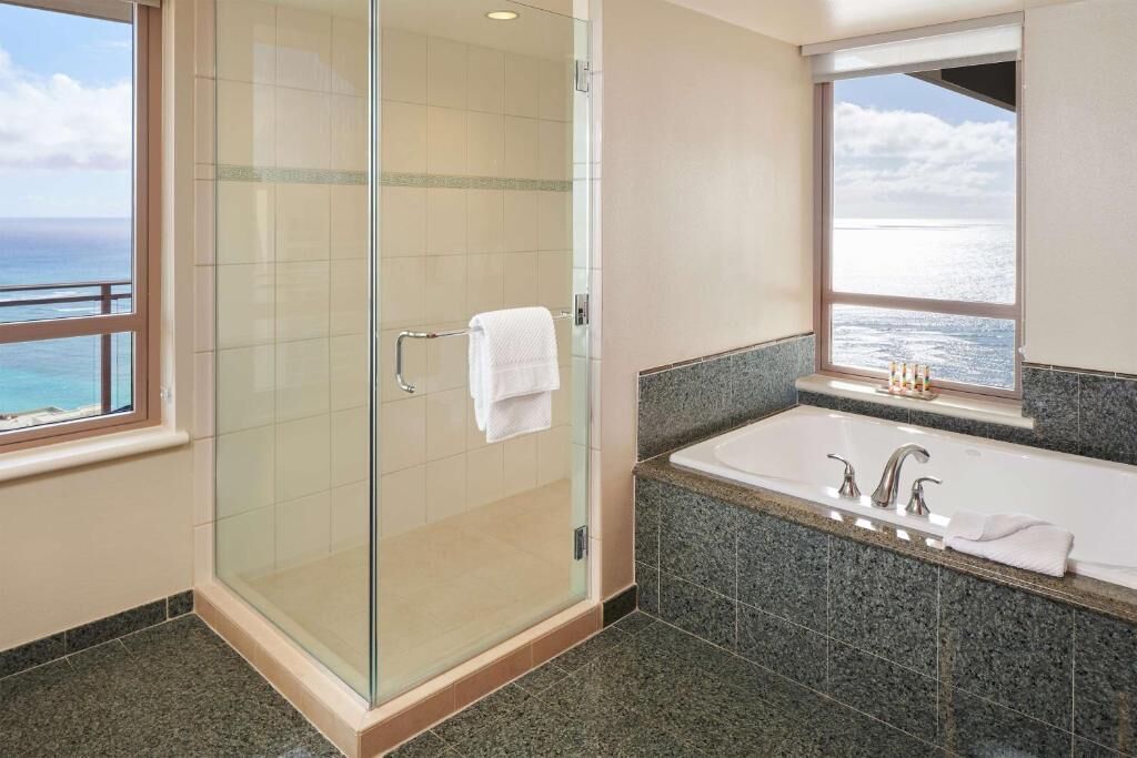 A modern bathroom with a glass-enclosed shower, a large bathtub, and a view of the ocean.