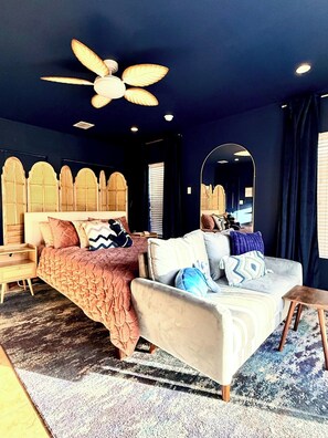 A bedroom with a bed, a sofa, a ceiling fan, a mirror, and a window with curtains. - MerManor - An Iconic Merman Pool Oasis (Fort Lauderdale)