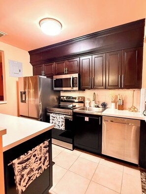 A kitchen with dark wooden cabinets, stainless steel appliances, and a white countertop. - MerManor - An Iconic Merman Pool Oasis (Fort Lauderdale)