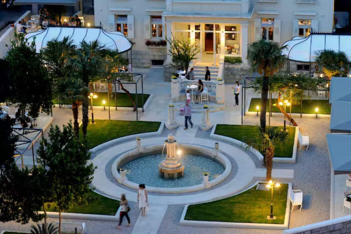 Un patio con una fuente central, rodeado de zonas de estar y palmeras.
