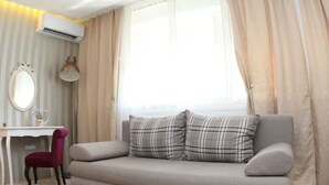 Una habitación moderna con sofá, escritorio, silla y un ventanal con cortinas.