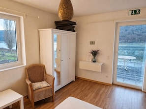 Ein Zimmer mit einem Korbstuhl, einem weißen Schrank, einem kleinen Tisch und Blick auf eine verschneite Landschaft durch eine Glastür.