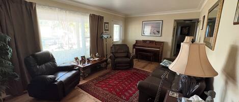 A living room with a piano, leather chairs, a red rug, and a lamp.