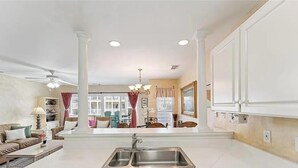 A spacious living room with a large window, a kitchen with a sink, and a dining area with chairs and a table. - Beach Block with ocean views in downtown Tybee Island (Tybee Island)