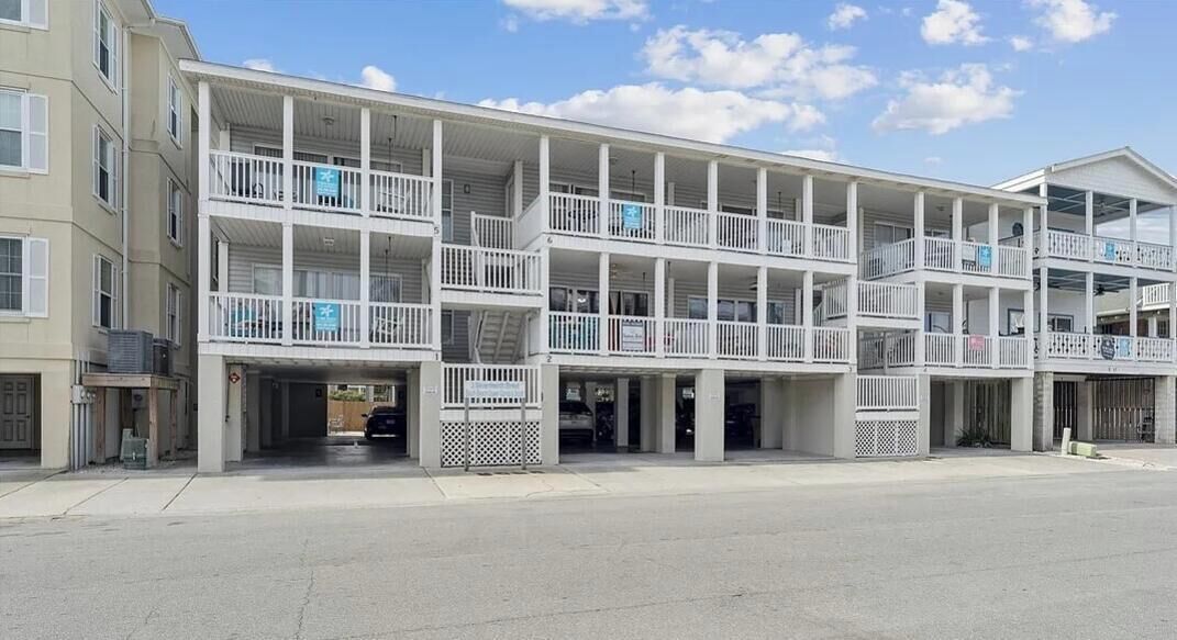 Un hotel de diversos pisos amb balcons, una zona de pàrquing coberta i un cel serè.