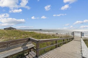 A wooden boardwalk leading to a beach with a pier in the background. - Beach Block with ocean views in downtown Tybee Island (Tybee Island)