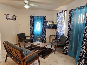 Ein Wohnzimmer mit einer Couch, Sesseln, einem Couchtisch, einem Fernseher und Vorhängen.