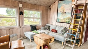 L’intérieur d’un chalet accueillant, avec un revêtement mural en bois, un canapé, une table basse, un fauteuil, une échelle et une bibliothèque.