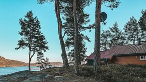Une cabane avec un toit rouge, entourée d’arbres et bordée par un plan d’eau.